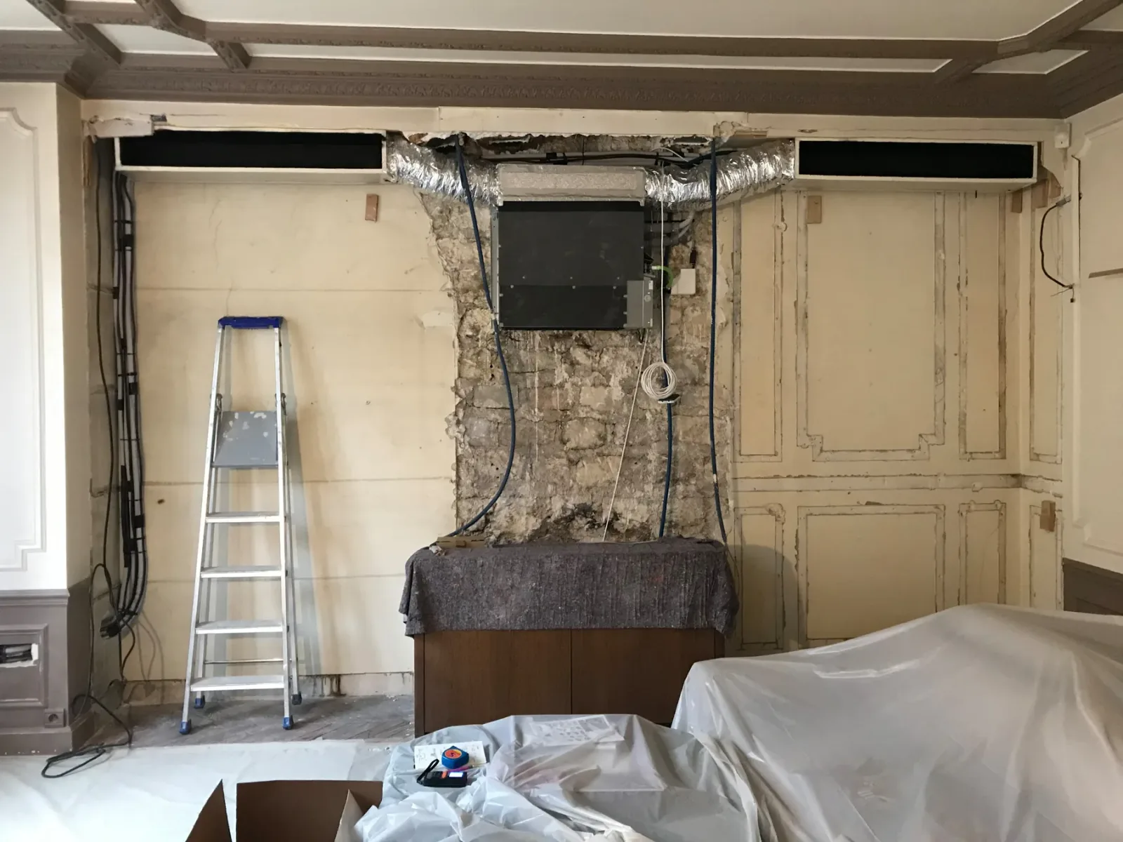 Avant travaux : gaine de climatisation et unité technique apparentes, câbles en attente, boiseries en partie déposées, escabeau et meubles bâchés