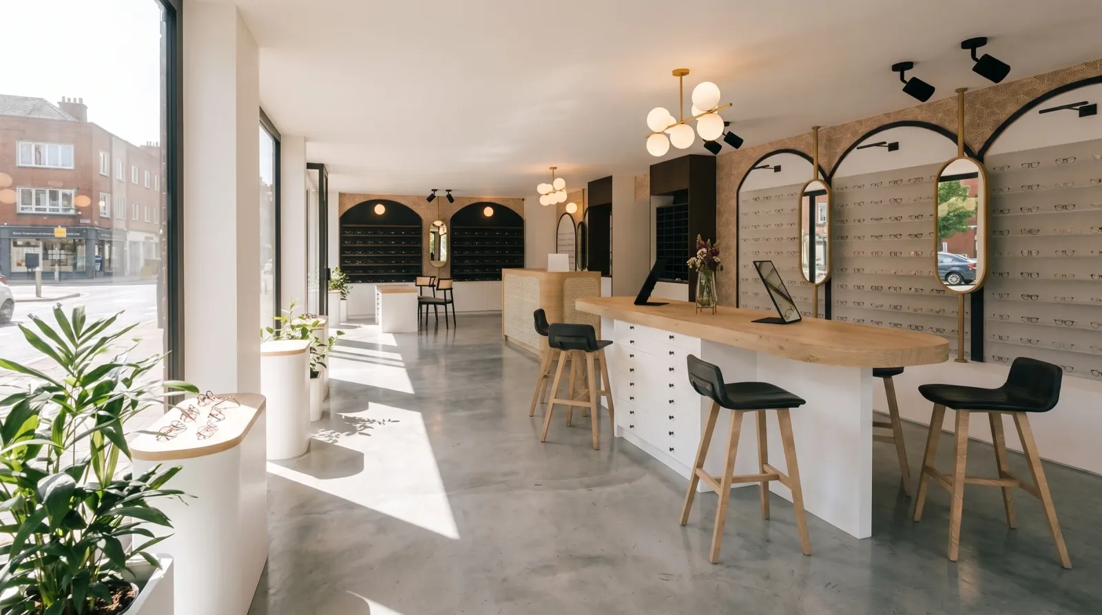 Le magasin d'optique en enfilade, présentoirs muraux à arches noires, table d'essayage centrale en bois clair avec tabourets, suspensions à globes de laiton et vitrine ouvrant sur la rue
