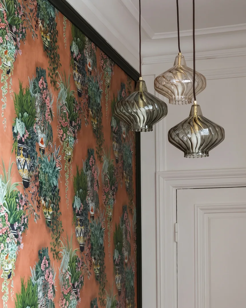 Panneau de papier peint panoramique orange encadré de noir et trois suspensions en verre fumé dans des bureaux aménagés dans un appartement haussmannien