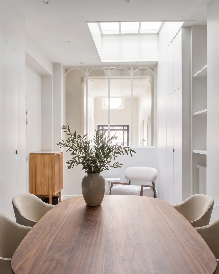 Salle de réunion de l'hôtel particulier : table ovale de noyer, fauteuils écrus, mur bleu nuit au-dessus d'un radiateur vert de gris et verrière blanche à arches sous la verrière de toit