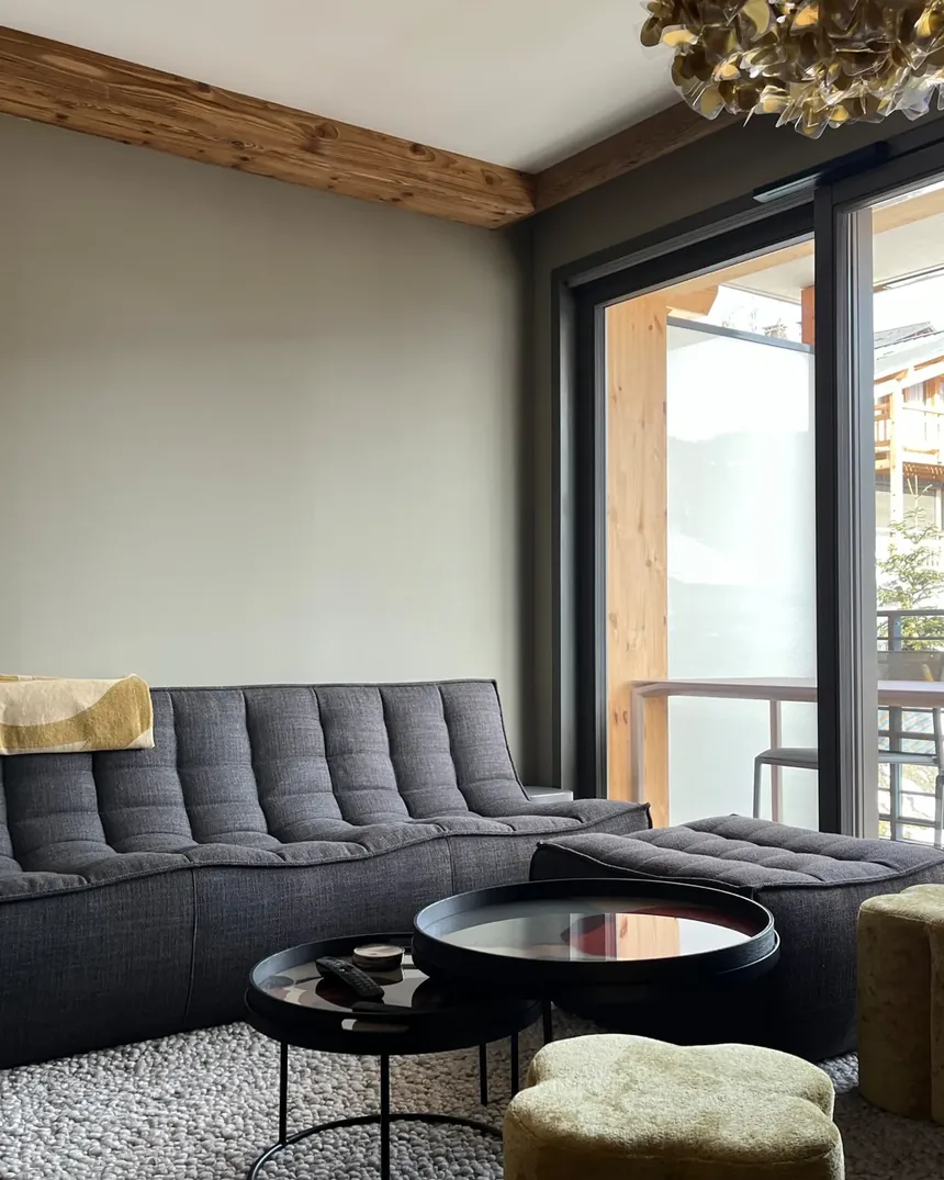 Séjour de l'appartement des Gets livré : canapé gris tourné vers la baie vitrée, aménagement conçu sur plan avant la livraison