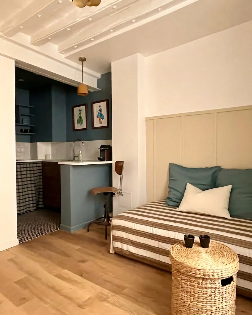 Le studio de 13 m² : kitchenette bleu canard derrière son muret, banquette à rayures et coussins bleus, panier en jonc et parquet clair