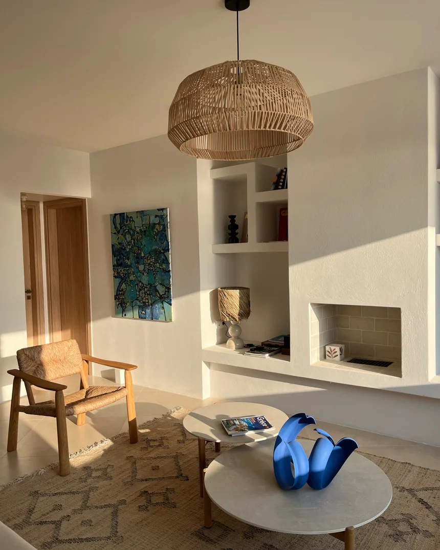 Le salon de la villa : suspension de rotin, fauteuil de bois et corde tressée, niches maçonnées blanches, cheminée et sculpture bleu vif sur la table basse